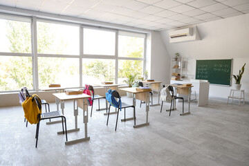 Interior of empty classroom with desks, backpacks on chairs and blackboard