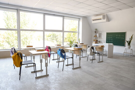 Interior of empty classroom with desks, backpacks on chairs and blackboard