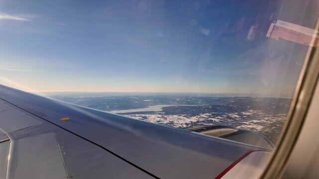 A view out the window of a Scandinavian Airlines aircraft flying low over a winter landscape on approach to Oslo Airport Gardermoen.