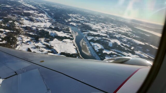 A view out the window of a Scandinavian Airlines aircraft flying low over a winter landscape on approach to Oslo Airport Gardermoen.