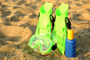 New swimming mask, flippers and sunscreen cream on sand © Pixel-Shot