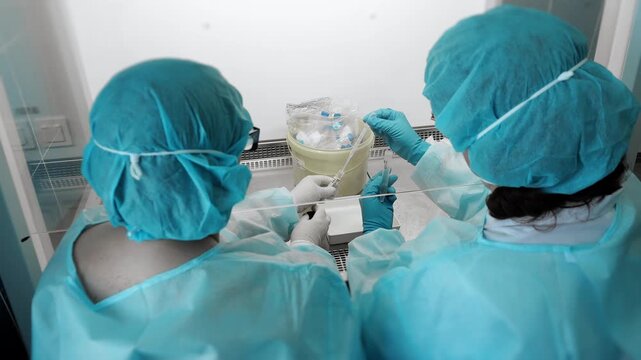 Top view of lab technicians working with biological samples using pipettes in sterile biosafety cabinet in clinical laboratory environment.