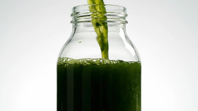 Green vegetable juice pouring into a clear glass bottle
