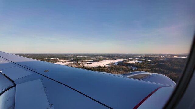 A view out the window of a Scandinavian Airlines aircraft flying low over a winter landscape on approach to Oslo Airport Gardermoen.