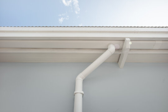 Perspective of white rain gutter system attached to building exterior. Ideal as background for technical content, product promotion and educational materials, modern rainwater drainage solution.