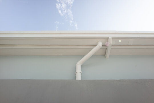 Building rainwater drainage system, PVC gutter supported by steel frame with connected downspout directing water to ground level drainage. Represent stormwater management and water flow control.