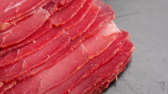 Thin slices of cured beef meat arranged in fanned layers on a dark surface.