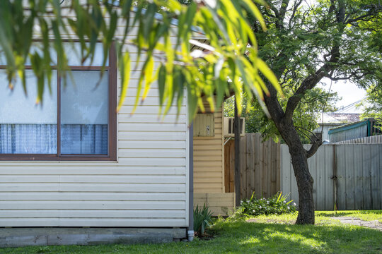 A modest weatherboard cottage or house exterior showcases horizontal cladding&nbsp;and humble metal gate. Practical materials and functional housing in suburban Australia.