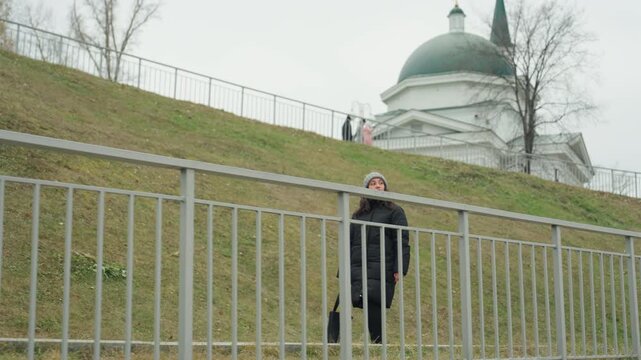 Woman on hill. Quiet woman standing near ancient dome. Woman reflects solitude on hilltop near old monument. Serene woman pauses on grassy hill adjacent to historic dome under cloudy sky