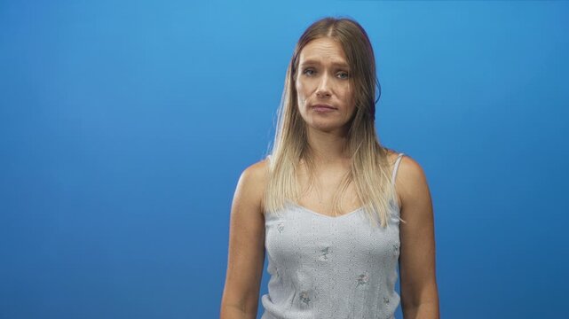 Woman face with subtle eye roll and tilted head, bare shoulders visible, wearing sleeveless top in blue studio; resignation reflection.