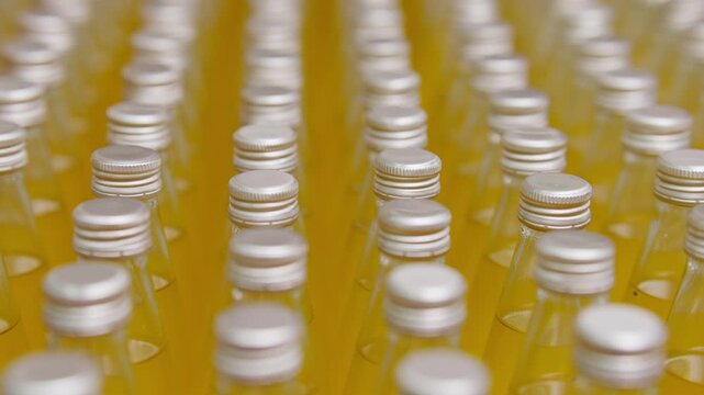 Bottled Beverages in Order: A close-up shot showcasing rows of transparent glass bottles, each sealed with a silver cap, filled with a vibrant orange liquid.