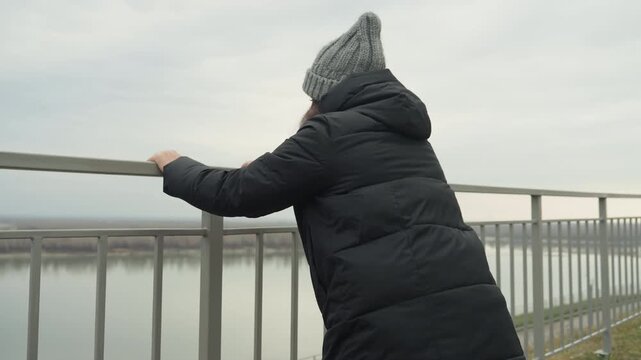 Latina dancer leaning on bridge railing overlooking river and horizon, puffer coat and beanie against overcast sky quiet contemplative pause with gentle balance and urban waterfront panorama, perfect