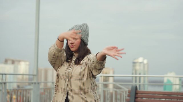 Skyline dance joy. Outdoor rehearsal with spirited dance and sweeping arm gestures. Dynamic rooftop performance capturing joyful expression with expansive gestures against hillside view