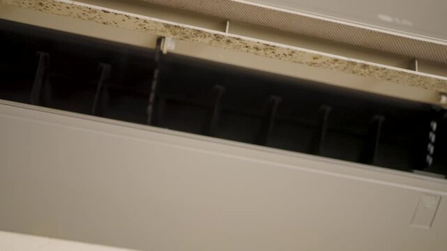 Close-up of Dirty Air Conditioner Vent with Mold and Dust. Split system air conditioner interior showing dust and mold accumulation on the fan blades and vent. Home maintenance and indoor air quality