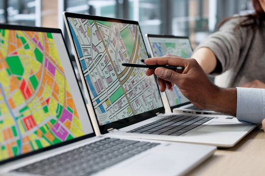 Two GIS Analysts Using Computers In Urban Office, Reviewing Cadastral Maps