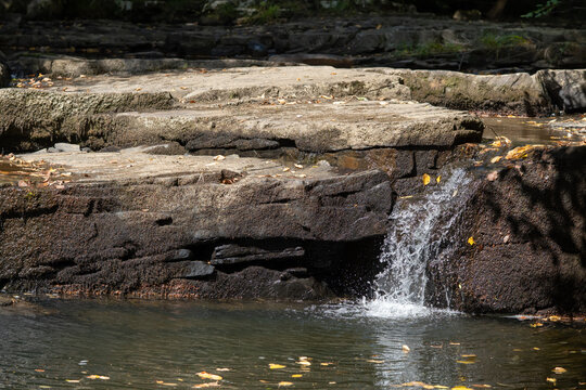 small waterfall flowing over a rock slab in a mountain stream at the start of the spring snow melt as meltwater rushes downstream towards the sea picking up sediment along the way