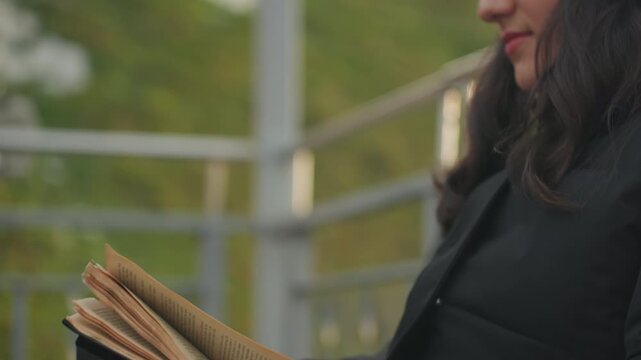 Young woman turning pages on bench at dusk, soft smile knit hat and warm jacket, closeup hands and face, narrative engagement and relaxed vibe, quiet park setting with subtle railing background