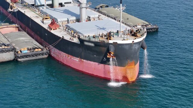 large cargo ship's bow discharging ballast water into the ocean. Maritime engineering operations, industrial shipping logistics, and environmental maintenance at sea.