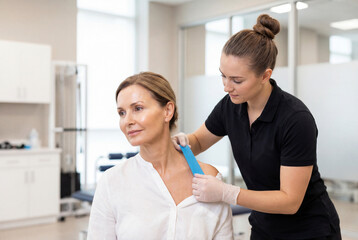 Fototapeta premium Female patient receiving kinesiology tape from physical therapist