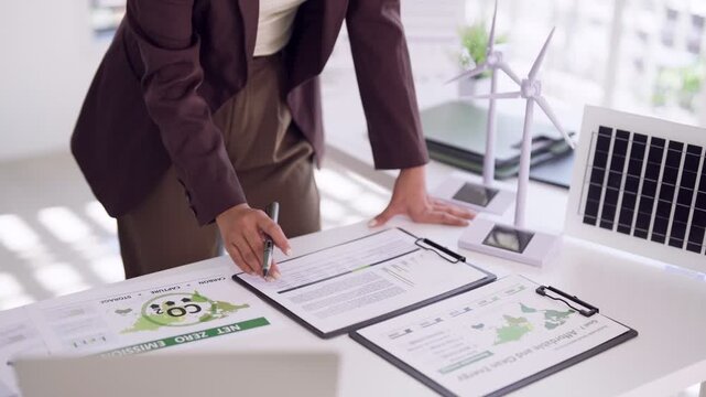 Asian adult woman professional analyzing sustainable energy reports for net zero emissions business strategy to achieve environmental goals in office