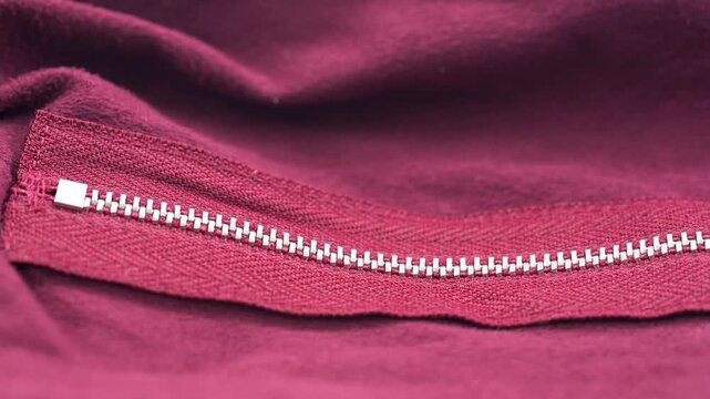 Close up of red fabric zipper with metal teeth and textile detail.