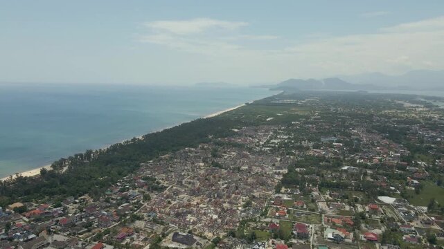 Wide aerial panorama of a coastal town settled between green hills and the sea.