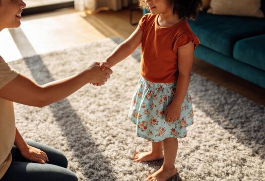 Little girl shaking hands with a new babysitter in a sunny living room for childcare services, professional introduction and greeting at home between adult and child