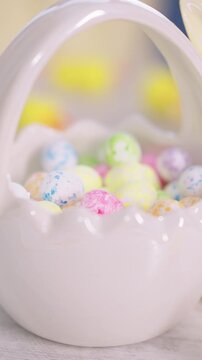 Tiny hand reaches for colorful candy eggs. Soft pastel hues fill a porcelain basket. Child's fingers gently explore sweet treats. Joyful discovery in a child's playful moment