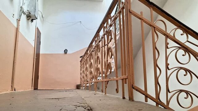 Indoor corridor with cracked concrete floor, reddish brown metal railing, and door view, highlighting architectural details, building condition, and structural wear