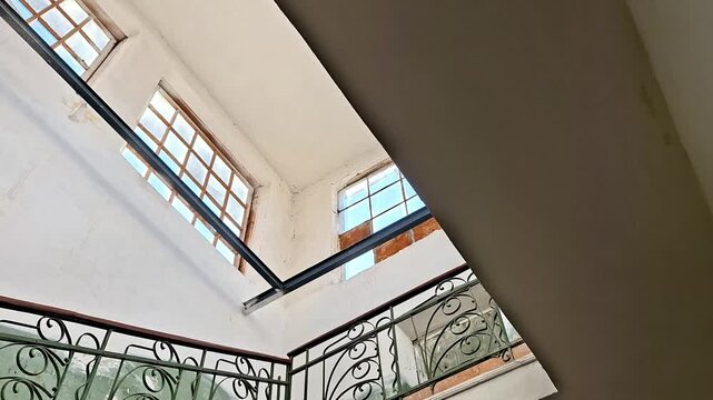 Old stairwell with ornate wrought iron railings and window light, highlighting vintage architecture, shadows, and upward perspective across multiple levels
