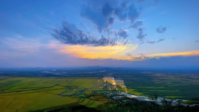 A serene landscape of green fields and a winding river at sunset with a blue sky and vibrant clouds