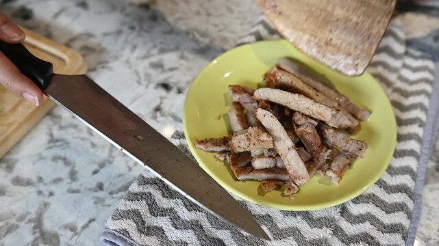 Transferring appetizing roasted pork chop slice from wooden cutting board to yellow plate brings joy and comfort inside bright cozy home kitchen preparing hearty meat dinner