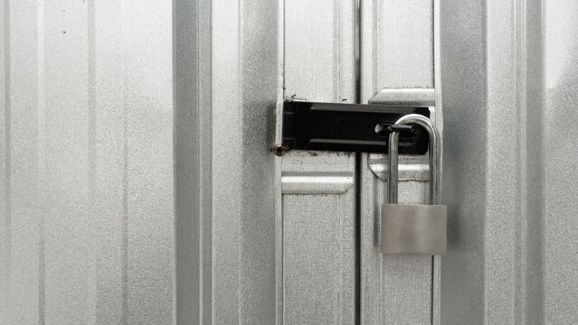Silver padlock securing a black metal latch on corrugated steel