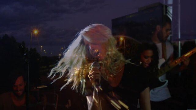 Lead singer leaning into mic causing hair-whip as city lighttrails melding stage energizing music