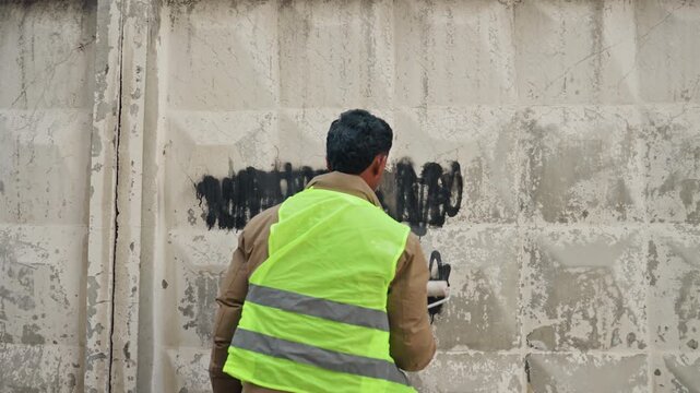 Individuals renew city surface. Maintenance crew systematically repaint vandalized city building surfaces. Skilled workers diligently apply new paint to cover graffiti and restore urban walls