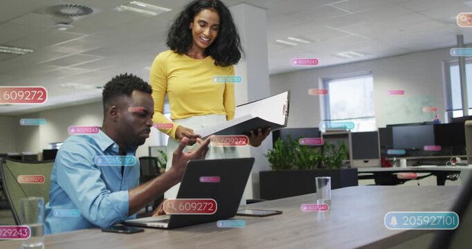 Coworkers at desk, woman pointing binder initiating animated UI tags on laptop aligning biz goals