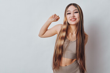 Fototapeta premium Young woman with long hair wearing a crop top and skirt standing against white background. Smiling female posing with raised arm and relaxed expression in studio setting.