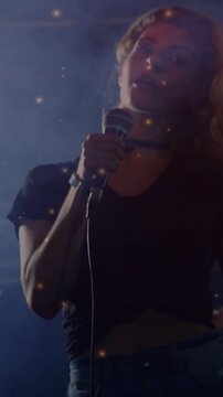 Vertical video: Female singer singing, holding mic, camera tilting up, particles shaping music mood