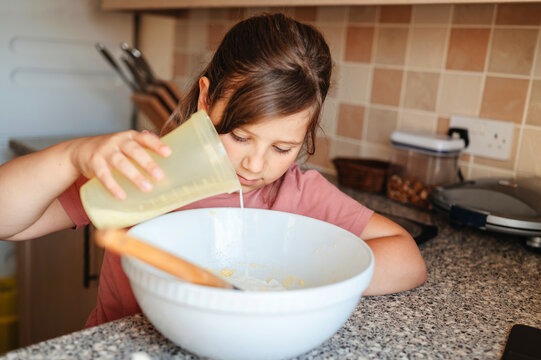 Girl pouring milk into bowl, baking, family cooking.