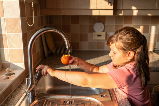 Girl washing fruit at kitchen sink, healthy habits.