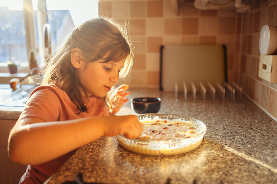 Girl spreading fruits on dough in kitchen, child cooking fruit pie.