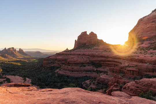 The sun flares as it sets behind rock formations