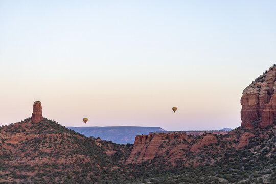 Hot air balloons rise over rocky forested landscape at sunrise