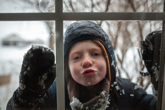 Playful child pressing face against window during snowy winter day