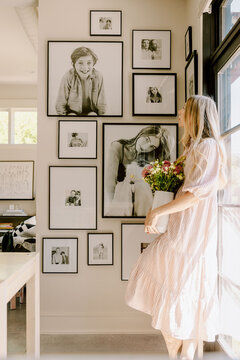 Woman admires gallery of framed portraits in her home