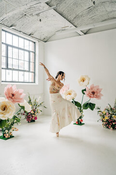 Ballerina dancing gracefully among giant spring flowers in studio