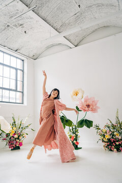 Dancer mid-leap among oversized flowers in bright studio