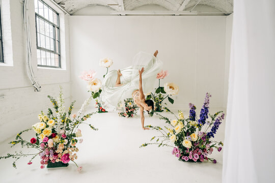 Dancer performing handstand with flowing dress among flowers
