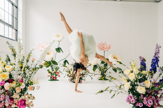 Woman performing handstand in blooming floral studio