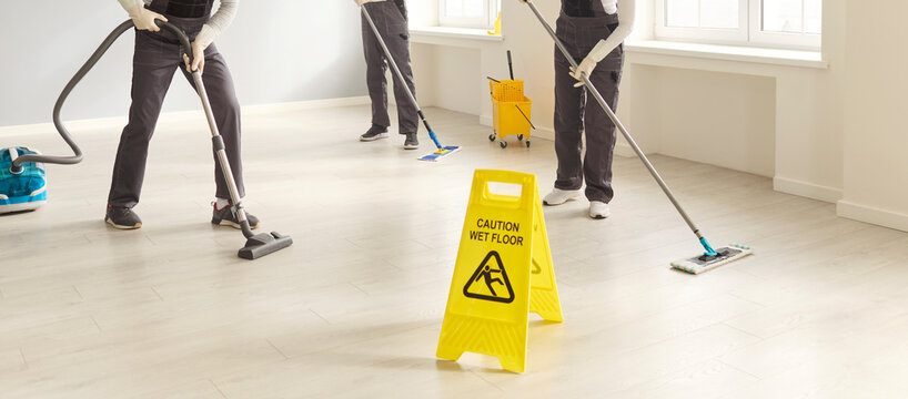 Cleaners team janitors mopping vacuuming sanitation safety. They maintain hygiene in a bright workplace with mops and a vacuum while a wet floor sign warns for safety. Clean team at a job.